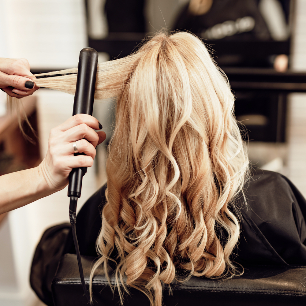 Stylist curling blonde hair with a flat iron at Salon LáShae in Kannapolis, NC